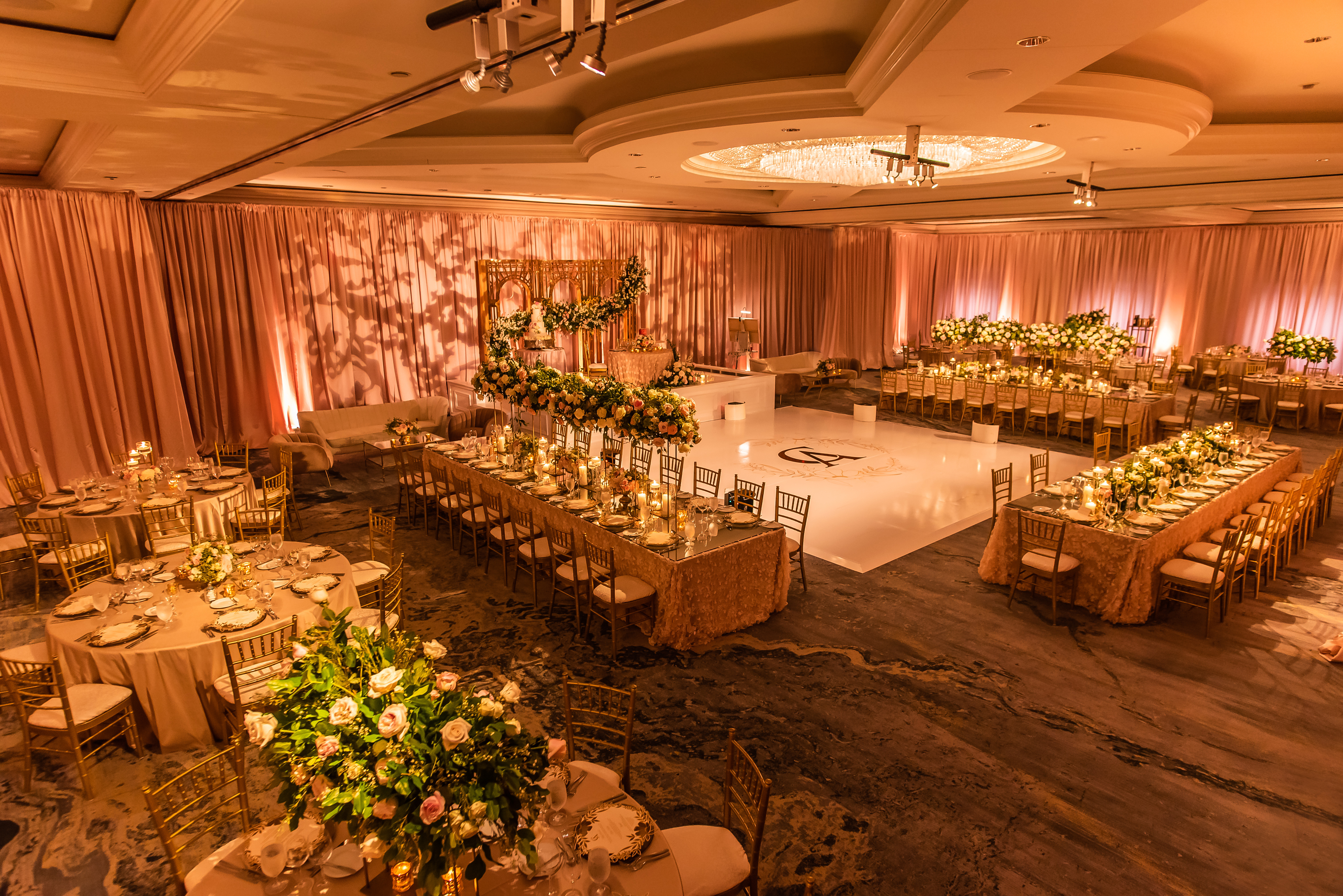 Grand luxury wedding venue with warm lighting, gold, peach, and blush tones creating an elegant and immersive atmosphere
