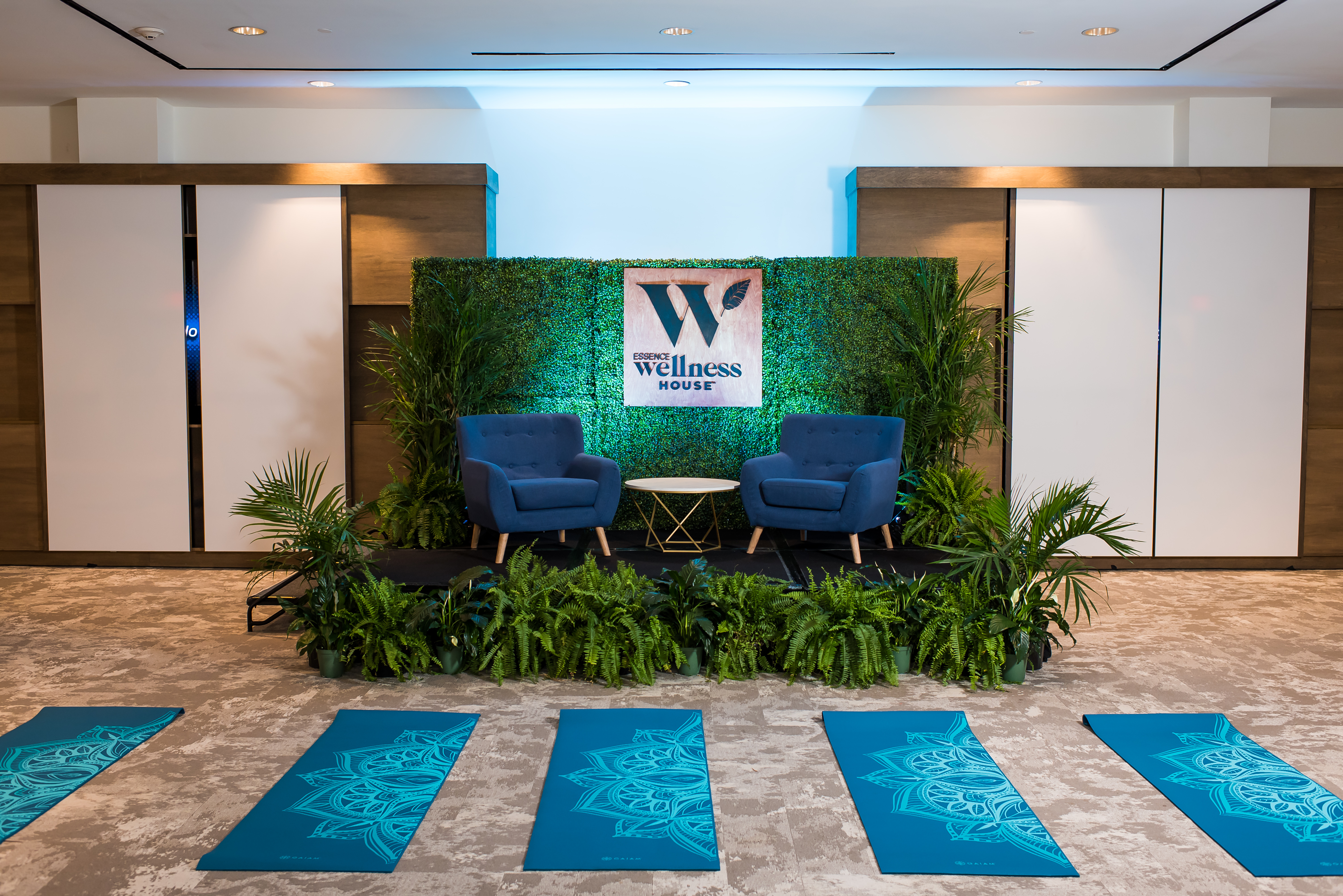 Wellness event setup with yoga mats, greenery, navy chairs, and a grass wall, showcasing a cozy and inviting color palette